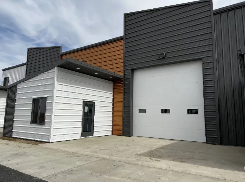 The Billings, Montana unit — a commercial building in white siding and dark steel with a cedar-clad entry bay, a glazed office door and a full-height overhead door.